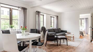 A modern living room with a dining area, large windows, and a view of greenery outside.
