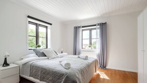 A bedroom with a bed, nightstands, a window with curtains, and a view of greenery outside. - Linneby , fri Parkering (Uddevalla)