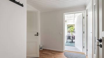 A hallway with a wooden floor, a white door, and a view of an outdoor patio area with chairs and a table.