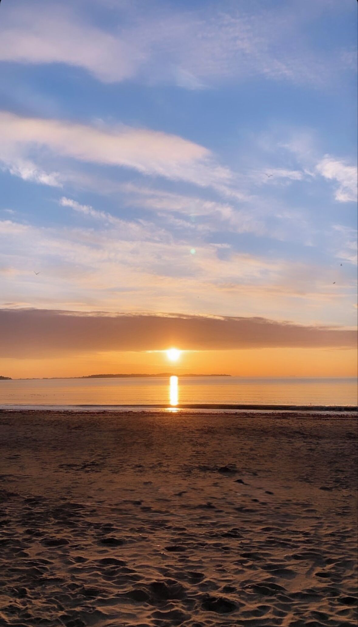 A beach with the sun setting over the horizon.