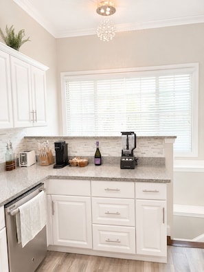 A kitchen with white cabinets, a granite countertop, a coffee maker, a blender, and a window with blinds. - Beautiful 3 bedroom house - Boston Beachside House Near Shore & Train (Revere)