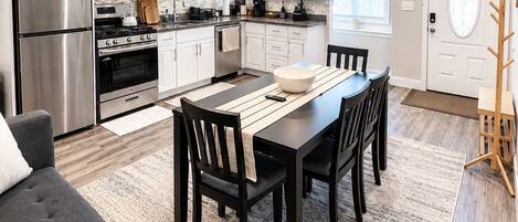 A modern kitchen with white cabinets, stainless steel appliances, and a dining area with a dark table and chairs.