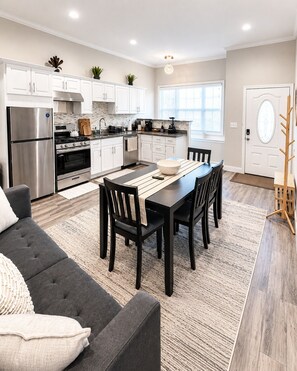 A modern kitchen with white cabinets, stainless steel appliances, and a dining area with a dark table and chairs. - Beautiful 3 bedroom house - Boston Beachside House Near Shore & Train (Revere)