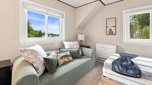 Quarto com cama, sofá, abajur e janela com vista para árvores.