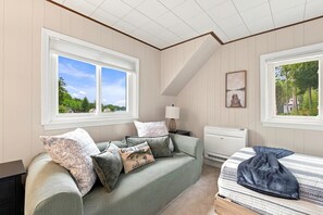 A room with a bed, a sofa, a lamp, and a window with a view of trees. - Lake Winnipesaukee Retreat | Private Beach | Dock (Alton)