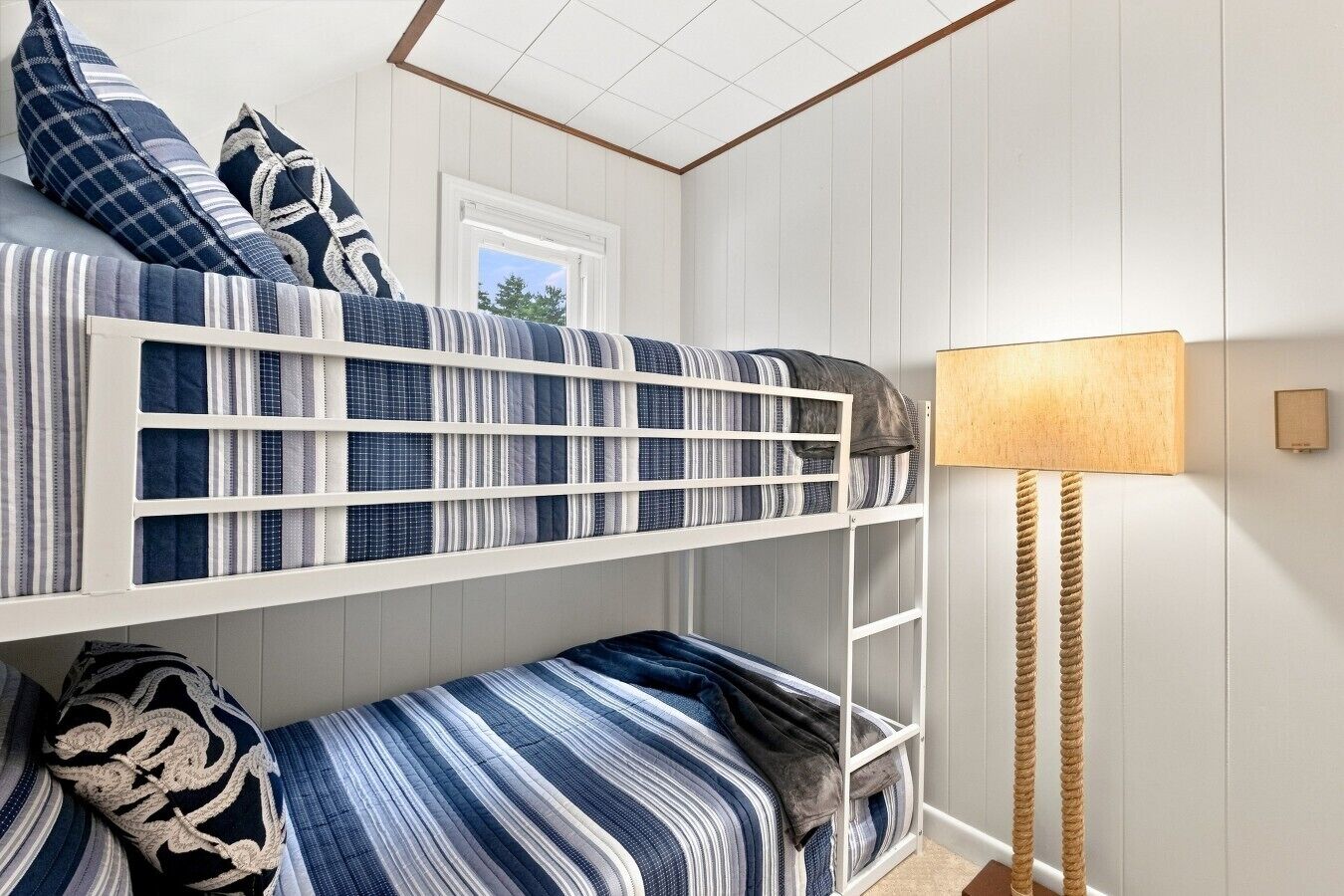 A bunk bed with striped bedding, a bedside lamp, and a window.