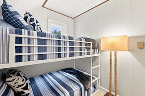 Una cama litera con ropa de cama a rayas, una lámpara de noche y una ventana.