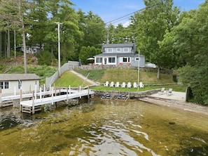 A lakeside property with a dock, a house, and a grassy area with chairs.