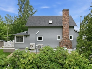 Una casa residencial con fachada gris, una chimenea de ladrillo y dos unidades de aire acondicionado.