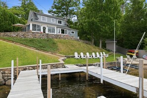 A house with a dock extending into a pond, surrounded by greenery and a stone wall. - Lake Winnipesaukee Retreat | Private Beach | Dock (Alton)