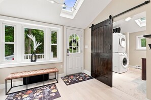 Un cuarto de lavandería con una puerta grande de madera oscura, una lavadora blanca y un banco con un tapete floral.