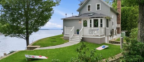 Een huis met twee verdiepingen, een veranda, een gazon en uitzicht op een waterpartij.