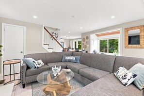 A modern living room with a sectional sofa, a glass coffee table, and a staircase leading to another level. - Lake Winnipesaukee Retreat | Private Beach | Dock (Alton)