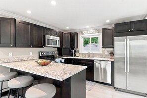 A modern kitchen with dark cabinets, stainless steel appliances, a marble countertop, and a central island with stools.