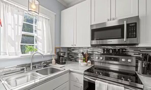 A modern kitchen with stainless steel appliances, a double sink, and a window with curtains. - Charming House in Port Royal Sleeps 5 (Port Royal)