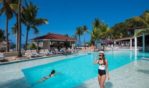 A pool area with lounge chairs and a small building, surrounded by palm trees. - Spacious 6-bedroom Villa within resort with private pool (Cofresi)