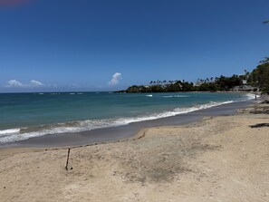 A beach with clear skies, calm waters, and a distant shoreline with buildings and trees. - Spacious 6-bedroom Villa within resort with private pool (Cofresi)