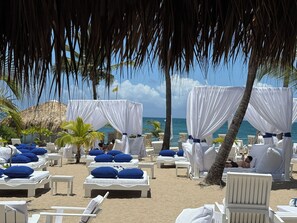 A beachside resort with multiple lounge chairs and beds, some with blue pillows, under white canopies. - Spacious 6-bedroom Villa within resort with private pool (Cofresi)