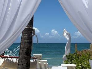 Une plage avec un hamac, une chaise blanche et une statue blanche.