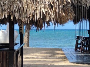 Une plage avec une structure dotée d’un toit de chaume, une terrasse en bois et une vue sur l’océan.