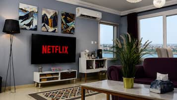 A living room with a flat-screen TV displaying 'NETFLIX,' a large window with a city view, and a potted plant.