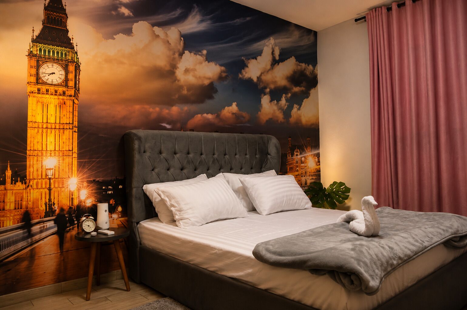 A bedroom with a large bed, a clock, a lamp, and a wall mural of a famous clock tower.