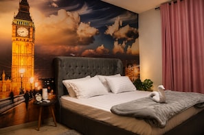 A bedroom with a large bed, a clock, a lamp, and a wall mural of a famous clock tower.