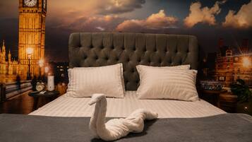A bed with a tufted headboard, two pillows, and a swan-shaped towel.