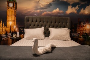 A bed with a tufted headboard, two pillows, and a swan-shaped towel.