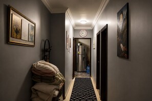 A hallway with a refrigerator, a clock, and artwork on the walls.