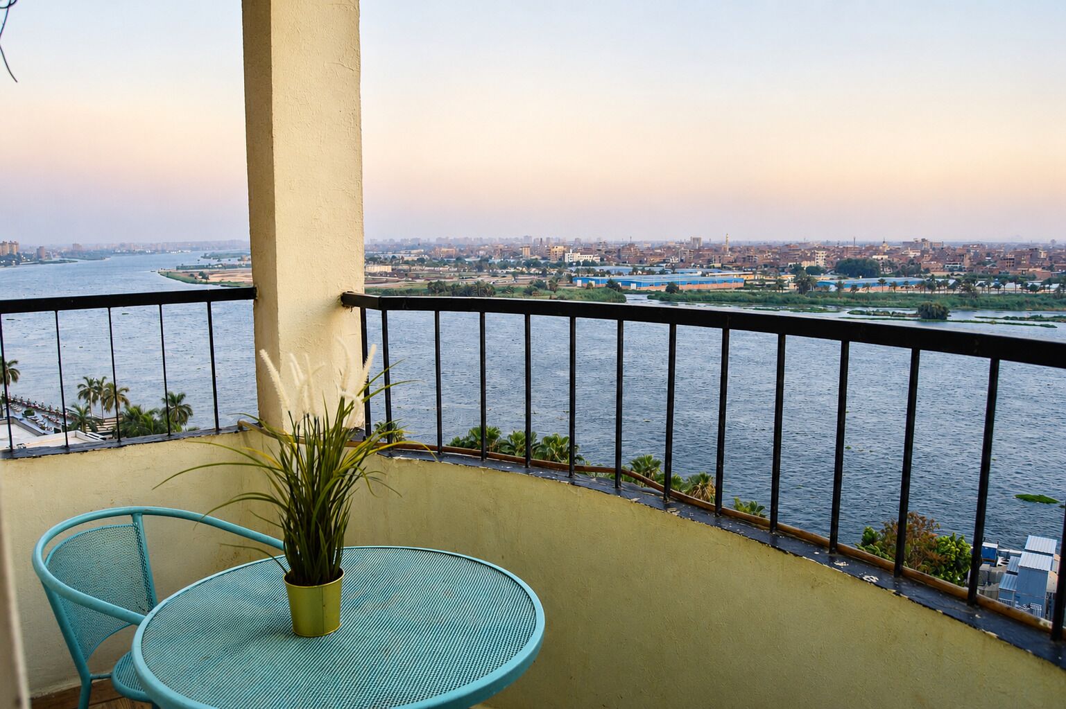 A balcony with a view of a river and cityscape, a round table, and two chairs.