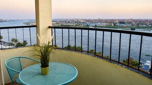 A balcony with a view of a river and cityscape, a round table, and two chairs.