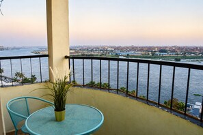 A balcony with a view of a river and cityscape, a round table, and two chairs.