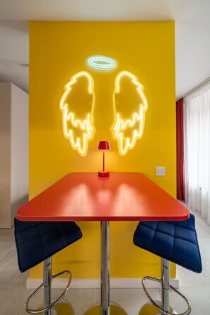 A dining area with a yellow accent wall, a red table, and two blue chairs. - Yellow Boom! (Sofia)
