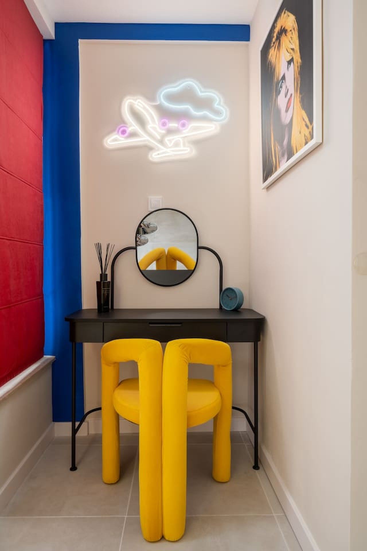 A room with a desk, two yellow chairs, a round mirror, a neon cloud light, and a framed picture on the wall.