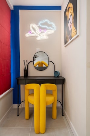 A room with a desk, two yellow chairs, a round mirror, a neon cloud light, and a framed picture on the wall. - Yellow Boom! (Sofia)