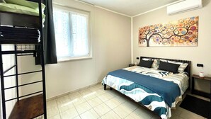 Quarto com beliche, janela com cortinas, cama com colcha estampada, ar condicionado e pintura na parede.