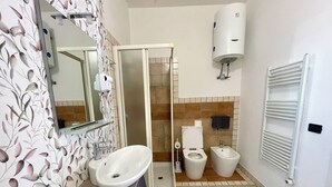 Casa de banho com lavatório, sanita, bidé, chuveiro e porta-toalhas.