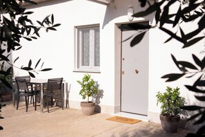 An outdoor seating area with a table and chairs, two potted plants, and a door with a doormat. - Cozy detached cottage near Assisi, Perugia, the airport, and the Umbria trade fairs (Bastia Umbra)