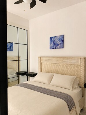A bedroom with a bed, a nightstand, a ceiling fan, a wall-mounted artwork, and a large mirror. - Luxury 1-Br Condo at Hard Rock Punta Cana — Resort Living, 15 mins from Downtown (Punta Cana)