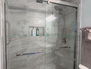 Eine begehbare Dusche mit Glaswänden, ausgestattet mit einer Duschbrause und einem Handbrauseinsatz.
