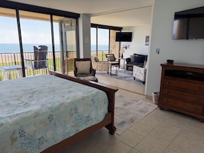 Een slaapkamer met een bed, een dressoir, een televisie en een balkon met uitzicht op zee.