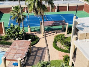 Uma quadra de tênis cercada por palmeiras e uma área de piscina.