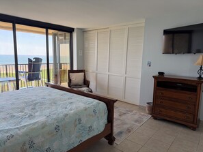 Quarto com cama, poltrona, cômoda e vista para o oceano através de uma porta deslizante.
