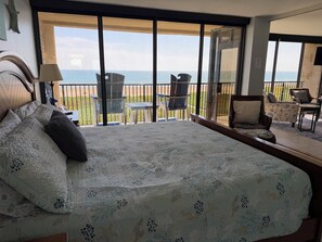 Ein Schlafzimmer mit einem großen Bett, Meerblick durch einen Balkon und einer Sitzecke mit Stühlen und Tisch.