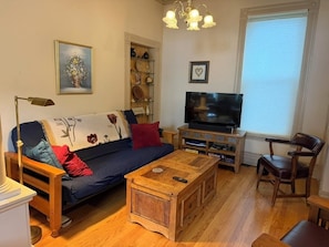 A living room with a sofa, coffee table, TV, and a chair. - 3-bedroom apartment with garage on welcoming Tipperary Hill in Syracuse (Syracuse)