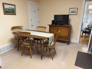 A dining area with a table and chairs, a television on a dresser, and a door leading to another room. - 3-bedroom apartment with garage on welcoming Tipperary Hill in Syracuse (Syracuse)