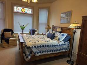 A bedroom with a bed, two chairs, a lamp, and a window with a stained glass design. - 3-bedroom apartment with garage on welcoming Tipperary Hill in Syracuse (Syracuse)