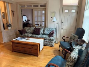 Sala de estar com sofá, mesa de centro e uma cadeira. Apresenta um armário de madeira e uma porta com painéis de vidro.