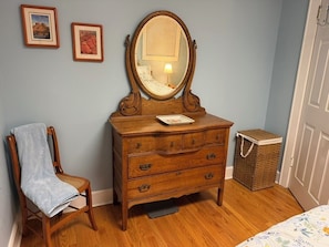 A wooden dresser with a mirror, a chair with a towel, and a wicker basket. - 3-bedroom apartment with garage on welcoming Tipperary Hill in Syracuse (Syracuse)